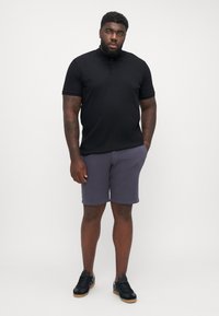 Korte ermer svart polo skjorte med krage, kombinert med grå shorts. Avslappet stil komplementert med svarte sneakers med gummisåler.