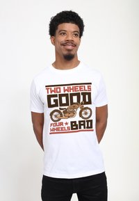 Camiseta blanca de algodón con un diseño gráfico que incluye el texto "DOS RUEDAS BUENO, CUATRO RUEDAS MALO" y una ilustración de una motocicleta en tonos marrones.