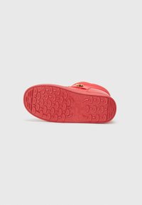 Red rubber shoe sole with textured patterns and grooves for traction, featuring a gold zipper accent and smooth upper surface.