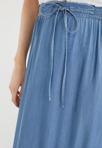 Jupe en denim bleu clair avec une texture douce, dotée d'une ceinture froncée et d'un cordon de serrage noué pour un ajustement réglable.