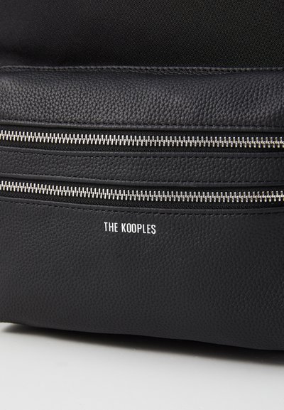 Fekete textúrájú bőrtáska, amelyet két ezüst cipzár díszít, és rajta fehér színű "THE KOOPLES" logó található, valamint sima anyagú belső térrel rendelkezik.
