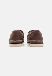 Braune Lederbootsschuhe mit goldenen Ösen, ausgestattet mit einer genähten Sohle und einem kontrastierenden weißen Gummiboden für besseren Halt.