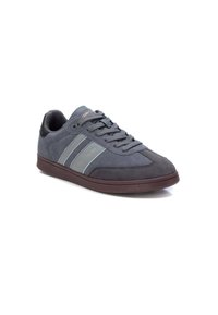 Zapatilla de ante gris con acentos en gris oscuro, dos rayas en gris claro a los lados y una suela de goma marrón. Presenta cordones redondos y un cuello acolchado.