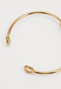 Gullfarget metallarmbånd med en glatt, avrundet design og to sirkulære detaljer i hver ende.
