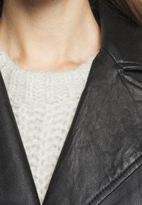 Black leather jacket collar layered over a white, chunky knit sweater. The sweater features a textured, patterned finish.