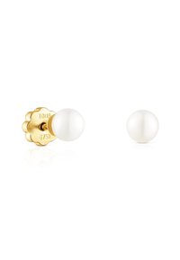 Pendientes de botón de tono dorado con perlas blancas. La parte trasera tiene un diseño escallopado, estampado con "TOUS" y "6750", lo que indica calidad.