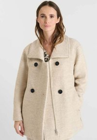 Abrigo de lana beige con corte relajado, que presenta un gran cuello, botones negros de doble botonadura y dos bolsillos laterales. Textura suave.