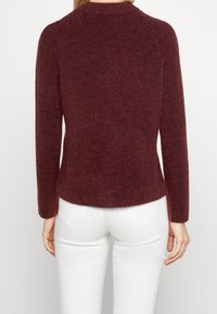Pull côtelé bordeaux à manches longues et encolure ronde, avec une texture douce et une coupe ajustée à la taille.