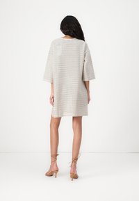 Vestido de manga curta, xadrez em bege claro e castanho escuro, com um corte descontraído e comprimento até ao joelho. Acompanhado por sandálias de salto beje.