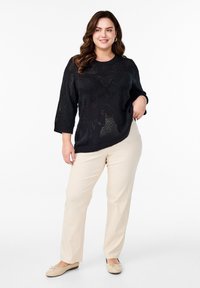 Pull en tricot noir avec un motif texturé, manches trois-quarts ; associé à un pantalon beige à jambes droites ; portant des ballerines de couleur claire.