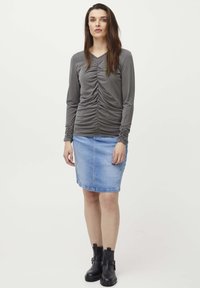 Langærmet, grå top med samlet og rynket front; parret med en lys blå denimnederdel; sorte ankelstøvler fuldender outfittet.