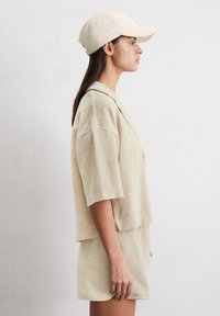 Completo in tessuto di spugna beige composto da un top a maniche corte e pantaloni shorts abbinati, accompagnato da un cappellino coordinato nello stesso materiale e colore.