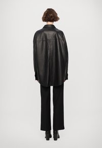Cămașă supradimensionată din piele neagră, cu guler, cusături pe umeri și tiv curbat. Asortată cu pantaloni negri cu croială dreaptă și botine cu toc.
