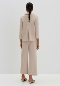 Completo beige su misura con un blazer dal taglio ampio, dotato di una fessura sul retro e pantaloni a gamba larga. Tessuto morbido con dettagli minimi.