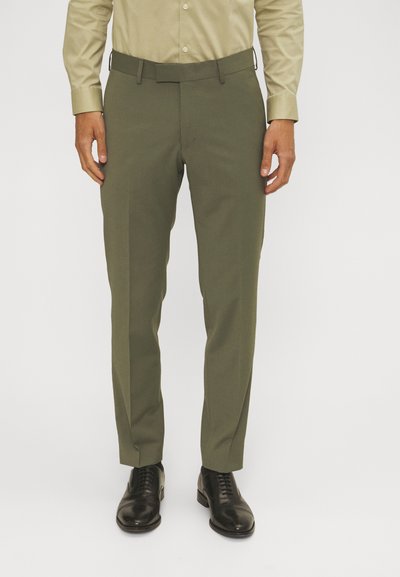 Olivgrüne Hosen mit glatter Textur, slim fit Design und flachem Bund. Kombiniert mit schwarzen Lederschuhen.