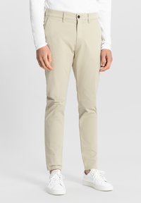 Beżowe chinosy o slim fit, z płaskim przodem, standardowymi kieszeniami i zapięciem na guzik. W połączeniu z białymi sneakersami.
