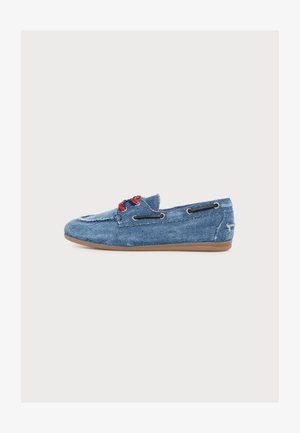 Mocassin en denim bleu avec des lacets rouges et des détails en lacets noirs sur les côtés, sur une semelle plate marron, vu de profil sur fond blanc.