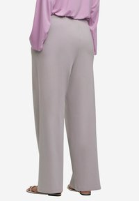Lichtgrijze, wijde broek van gladde stof. Heeft een elastische tailleband en een rechte snit, gecombineerd met lichte sandalen.