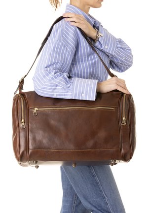 Borsa da viaggio in pelle marrone con doppi scomparti con cerniera, accessori in tonalità dorata e robusta tracolla. Texture liscia e forma arrotondata.