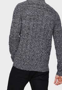 Gestrickter Pullover in Schwarz und Weiß, der ein strukturiertes Muster und einen hohen Kragen aufweist. Die Rückansicht zeigt schmal geschnittene Ärmel und einen Saum.