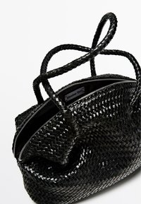 Borsa a tracolla in pelle intrecciata nera con superficie testurizzata, caratterizzata da due manici intrecciati e una chiusura con zip argentata sulla parte superiore.