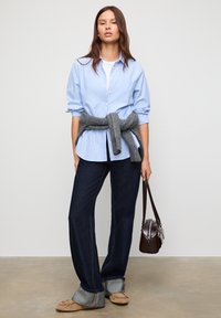 Light blue striped shirt, gray sweater tied at waist, dark denim jeans, tan slip-on shoes, and a small brown handbag. Simple and casual outfit.