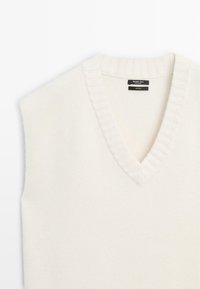 Hvid ærmeløs sweater i blød uld med dyb V-hals og ribbet detalje langs halsudskæringen. Glat tekstur med minimalistisk design.