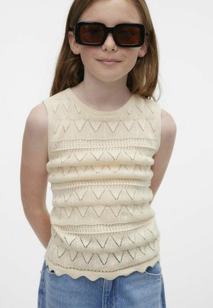 Beige knitted sleeveless top with a scalloped hem and zigzag pattern; lightweight fabric with a textured finish. Black oversized sunglasses.