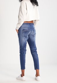 Jeans-joggers i medelblått, med en åtsittande design, femfickorsstil och elastiska muddar. Bärs med en kortärmad grå sweatshirt.