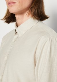 Beige overhemd met kraag en knoopsluiting, met een zachte textuur en subtiele glans, met strakke lijnen en zonder zichtbare patronen.