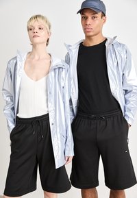 Des vestes de pluie argentées réfléchissantes sur des shorts noirs ; le modèle à gauche porte un haut côtelé blanc, celui de droite un t-shirt noir. Tenue décontractée pour l'extérieur.