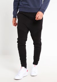 Pantalones de chándal negros con acentos acanalados en los muslos, ajuste entallado y tejido suave. Combinados con zapatillas blancas para un contraste.