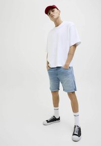 Hvid oversized T-shirt, lyseblå denimshorts med opslåede kanter, sorte sneakers med hvide såler og rød kasket. Simpelt design, afslappet look.