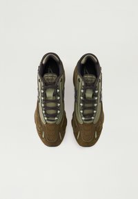 Olive green and brown athletic sneakers with mesh and suede materials, featuring a thick sole and contrasting laces. Brand logo visible.