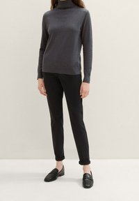 Grauer Rollkragenpullover, Strickstruktur, kombiniert mit schwarzen Slim-Fit-Hosen und schwarzen Slippers. Einfaches, tailliertes Design, lange Ärmel und umgeschlagene Bündchen.