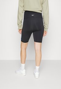 Calções de ciclismo pretos de cintura alta com uma textura suave, apresentando um logo branco horizontal nas costas e painéis laterais em contraste.