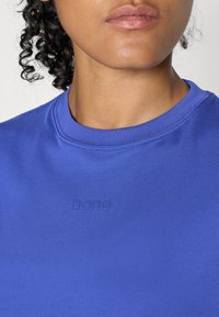 Kék pamut póló bordázott kerek nyakkivágással és dombornyomott "BORG" logóval az elülső részen. Sima textúrájú, testhezálló fazonnal.