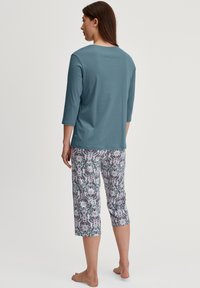 Tegen groene top met driekwart mouwen, gecombineerd met cropped broeken met een bloemenpatroon in roze, blauw en grijze tinten. Zachte stof, comfortabele pasvorm.