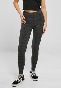 Leggings noirs et gris avec un motif à carreaux texturé, coupe ajustée, taille haute, associés à des baskets noires et blanches.