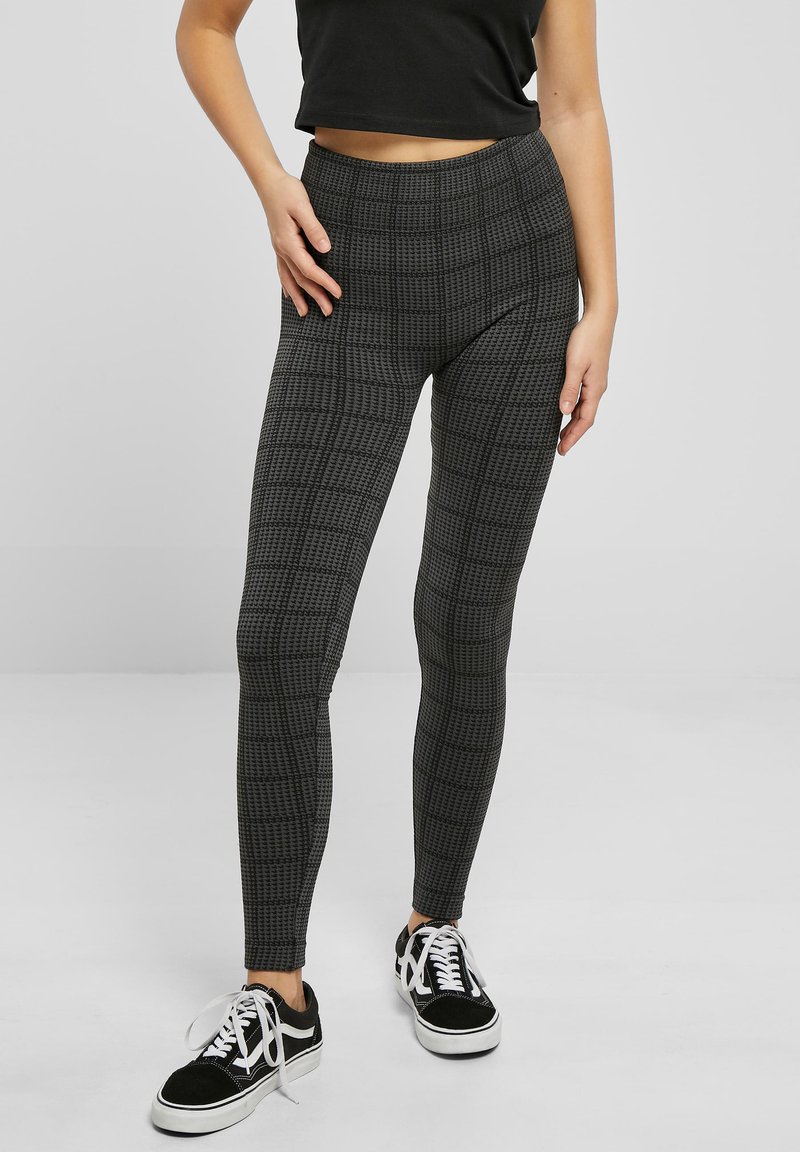Leggings noirs et gris avec un motif à carreaux texturé, coupe ajustée, taille haute, associés à des baskets noires et blanches.
