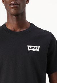 Melnas apģērbs ar apaļu kaklu, izgatavots no kokvilnas, ar baltu Levi's logo kreisajā krūtī. Gluda auduma, ar īsām piedurknēm.