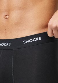 Zwarte boxershorts met een snug fit, voorzien van een tailleband gemarkeerd met "SNOCKS" in het wit. Gladde stoftextuur en geen zichtbare patronen.