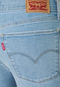 Jeans de mezclilla azul claro con un parche de cuero con marca roja, diseño de cinco bolsillos y costuras curvadas distintivas en los bolsillos traseros.