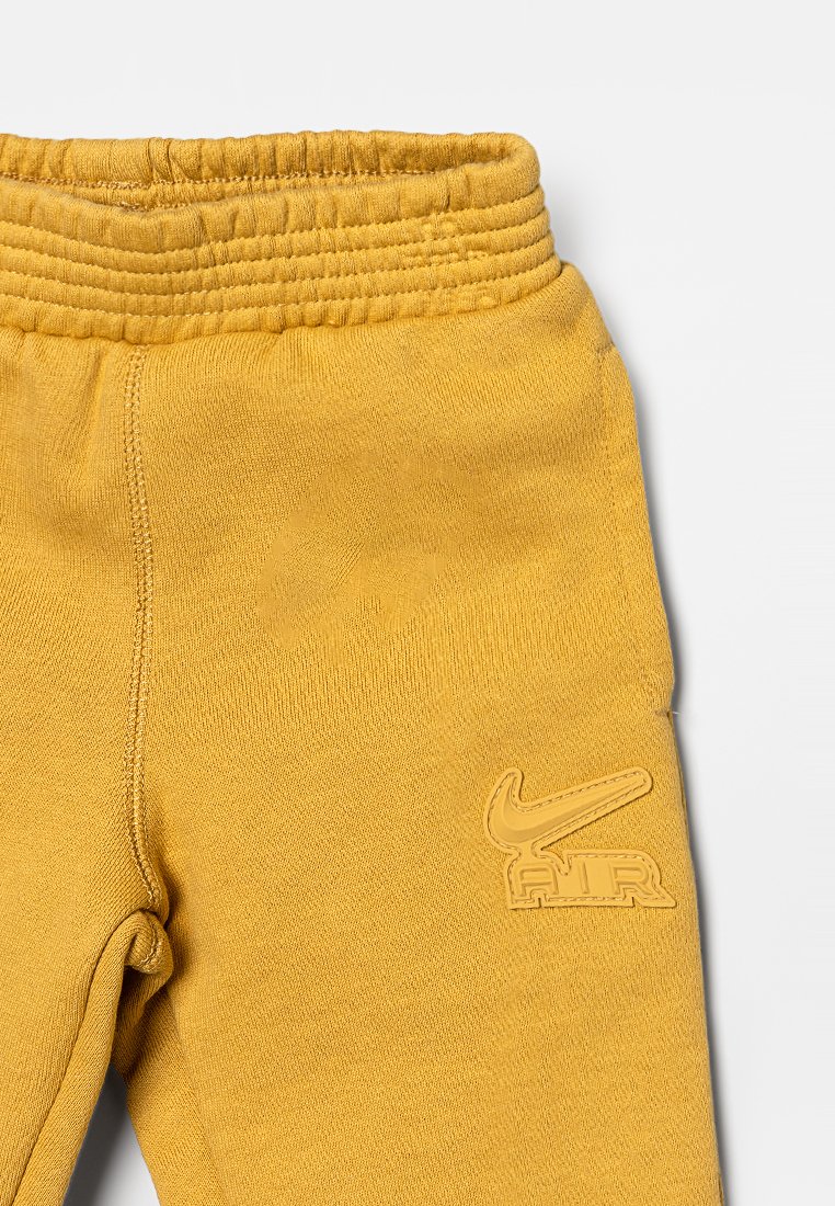 Pantalon de survêtement jaune avec une ceinture élastique texturée et un logo Nike Air en relief sur la cuisse gauche. Tissu doux et design ajusté.