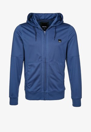 Marineblå hættetrøje med lynlås, snor i hætten, to sidelommer, ribkanter ved ærmerne, glat stof og en lille logo på brystet.