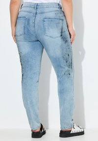 Jeans de denim de lavado claro con corte ajustado, que cuentan con dos bolsillos traseros y un patrón desgastado a lo largo de los lados. Acabados con un desvanecimiento sutil.