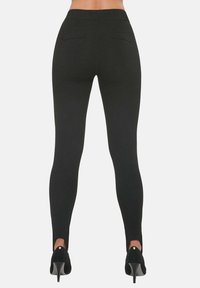 Czarne legginsy o dopasowanym kroju z wysokim stanem, tylnymi kieszeniami i wycięciami w okolicy kostek, zestawione z czarnymi szpilkami.
