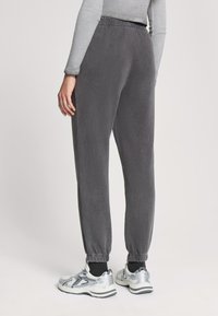 Szare spodnie dresowe z elastycznym pasem i ściągaczami. Miękka tkanina o gładkiej fakturze. W połączeniu z srebrnymi butami sportowymi.