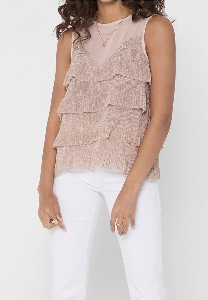 Haut sans manches rose clair avec des volants superposés, fabriqué en tissu texturé. Comprend un décolleté transparent et un ourlet légèrement irrégulier. Associé à un pantalon blanc.