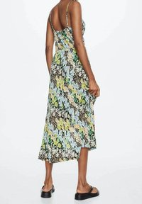 Monivärinen kukkakuvioinen maksimekko, jossa on istuva yläosa, ohuet säädettävät olkaimet ja hulmuava siluetti, jossa on etuosaa lyhyempi helma.